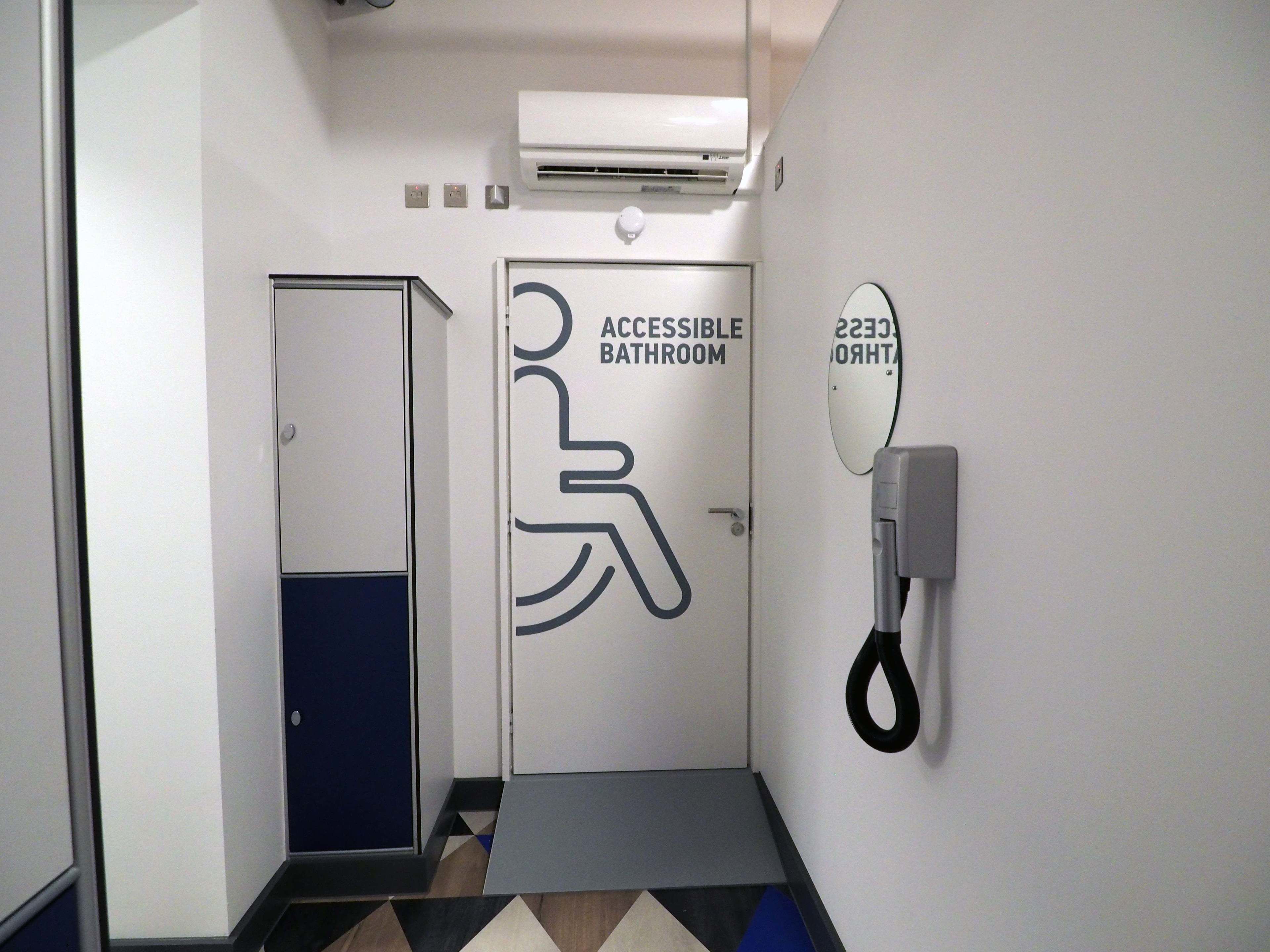 An accessible bathroom with a wheelchair symbol, a handrail, and a mirror on the wall.