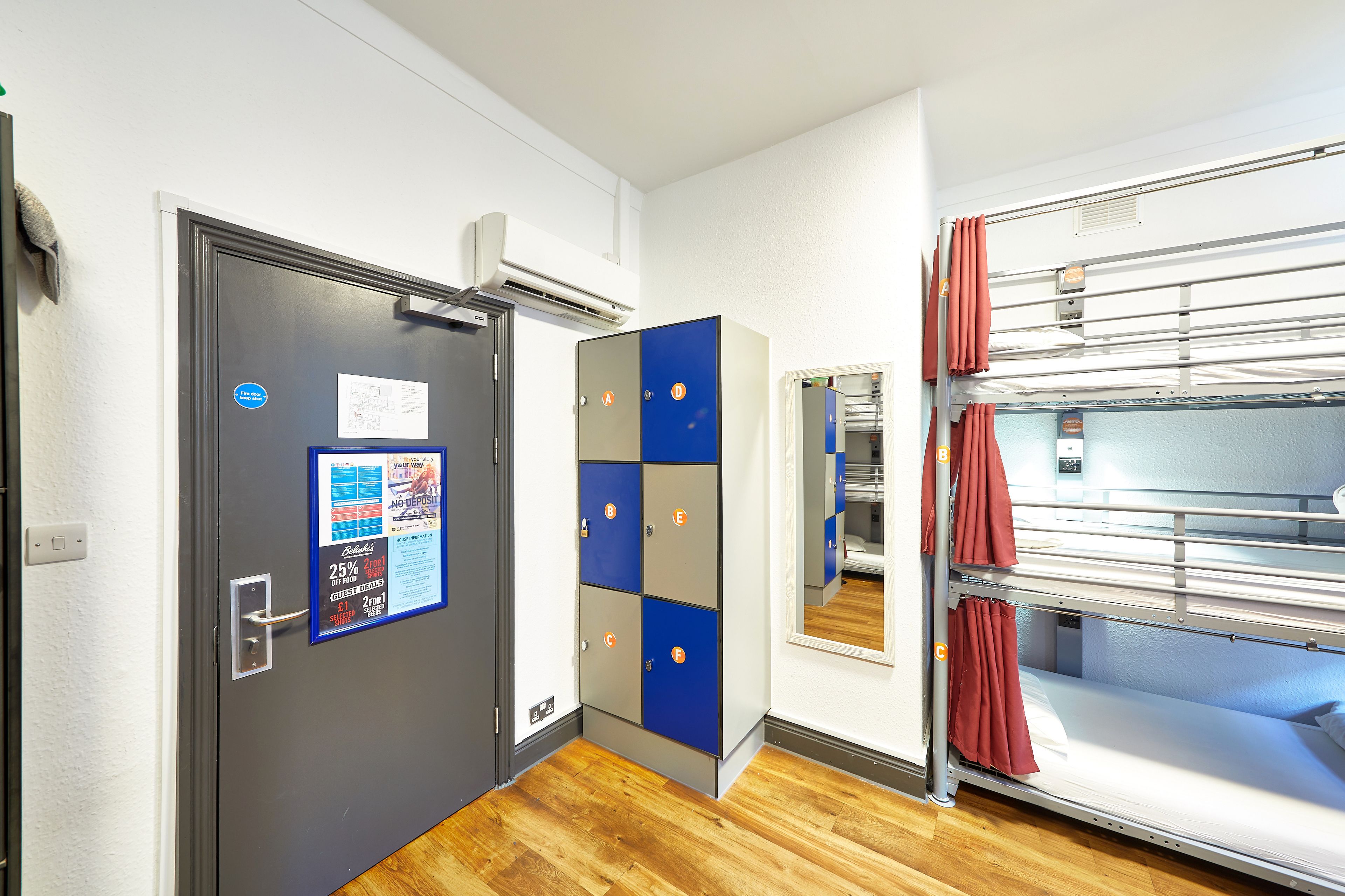 A hotel room with a bunk bed, a door with a bulletin board, and an air conditioning unit.