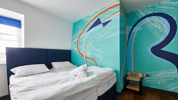 A modern hotel room with a neatly made bed, a blue headboard, and a large abstract mural on the wall.