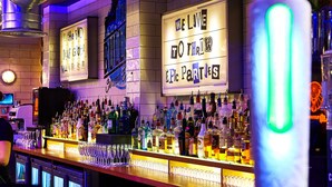 A bar with a variety of liquor bottles and glasses. There are illuminated signs on the wall. - St Christopher's Village, London Bridge - Hostel (London)