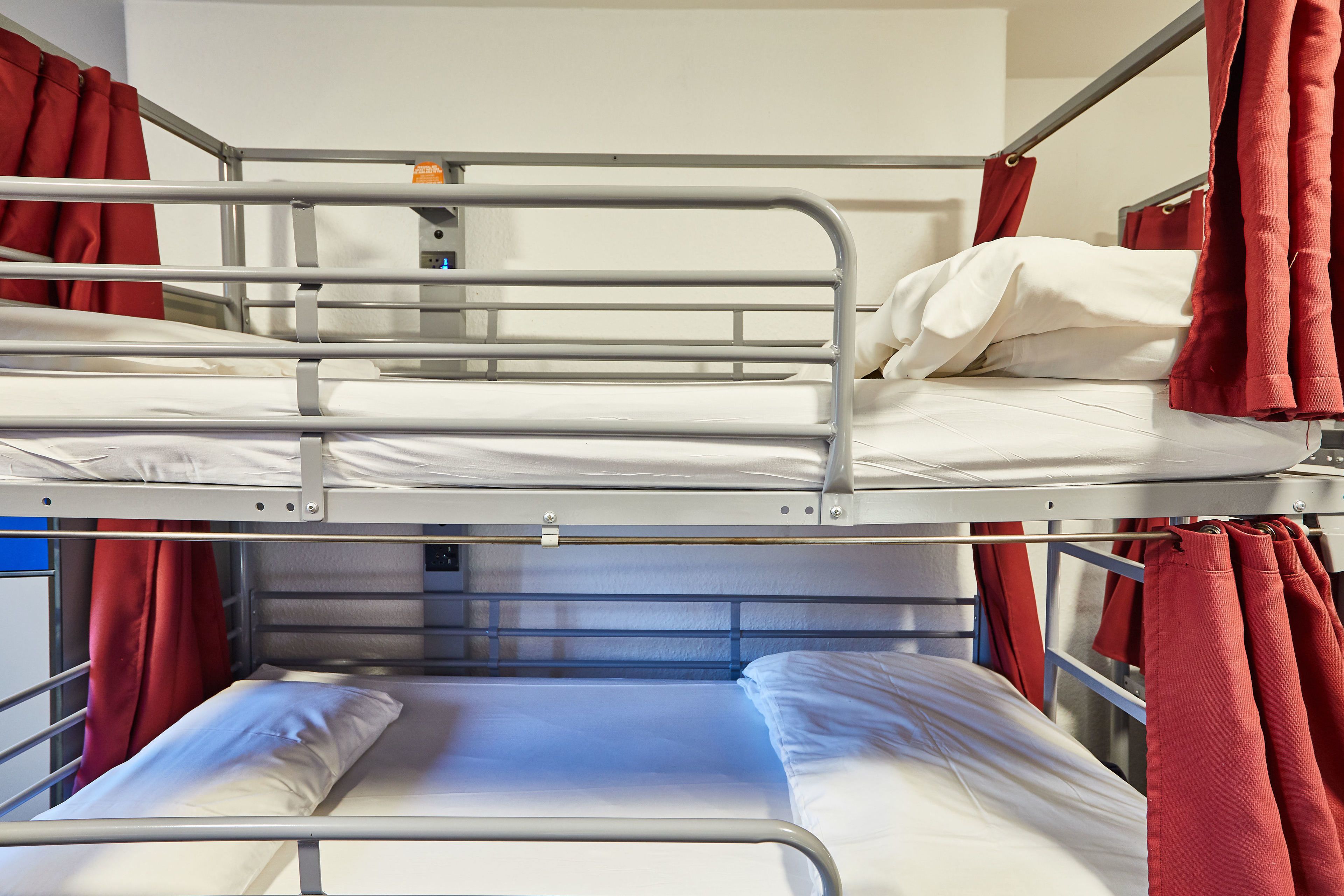 Una cama litera con barandillas de metal, cortinas rojas y ropa de cama blanca.