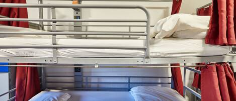 Una cama litera con barandillas de metal, cortinas rojas y ropa de cama blanca.
