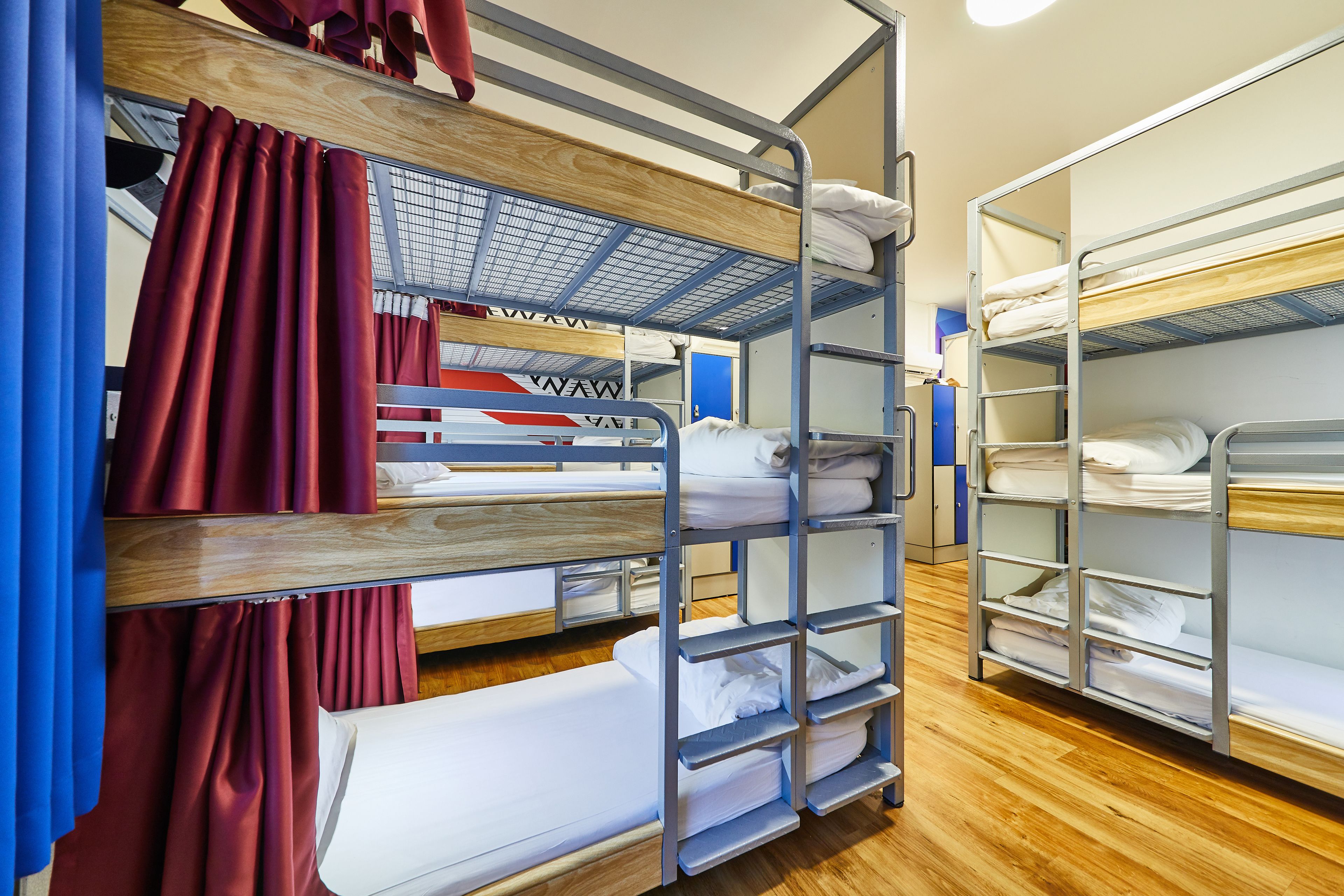 A bunk bed room with wooden and metal bunk beds, red curtains, and a blue door.