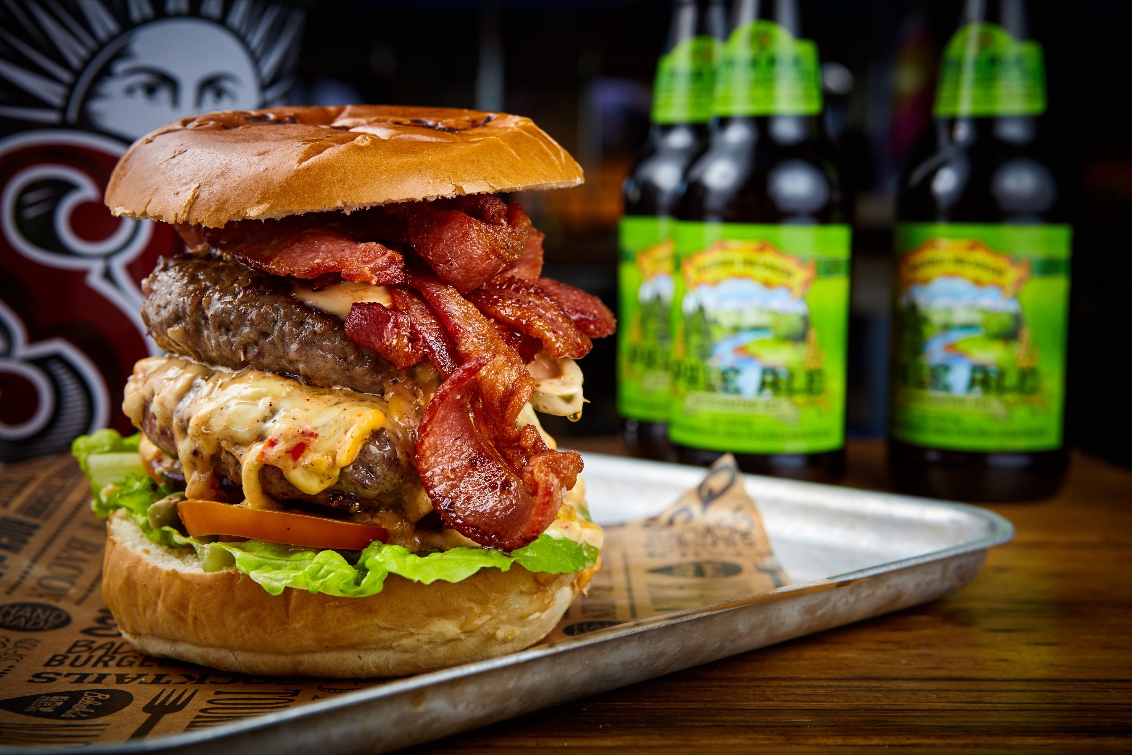 A burger with bacon, cheese, and lettuce on a bun, placed on a tray.
