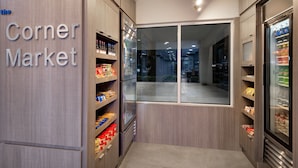 A corner market with wooden shelving stocked with snacks and beverages, a refrigerator, and a window offering a view of the street. - Fairfield Inn & Suites by Marriott Wilson (Wilson)