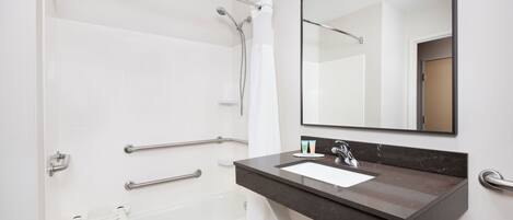 A modern bathroom with a bathtub, a vanity with a sink, a mirror, and a shower area with grab bars.