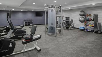 Ein Fitnessstudio mit Laufbändern, Krafttrainingsgeräten und einer Hantelbank.