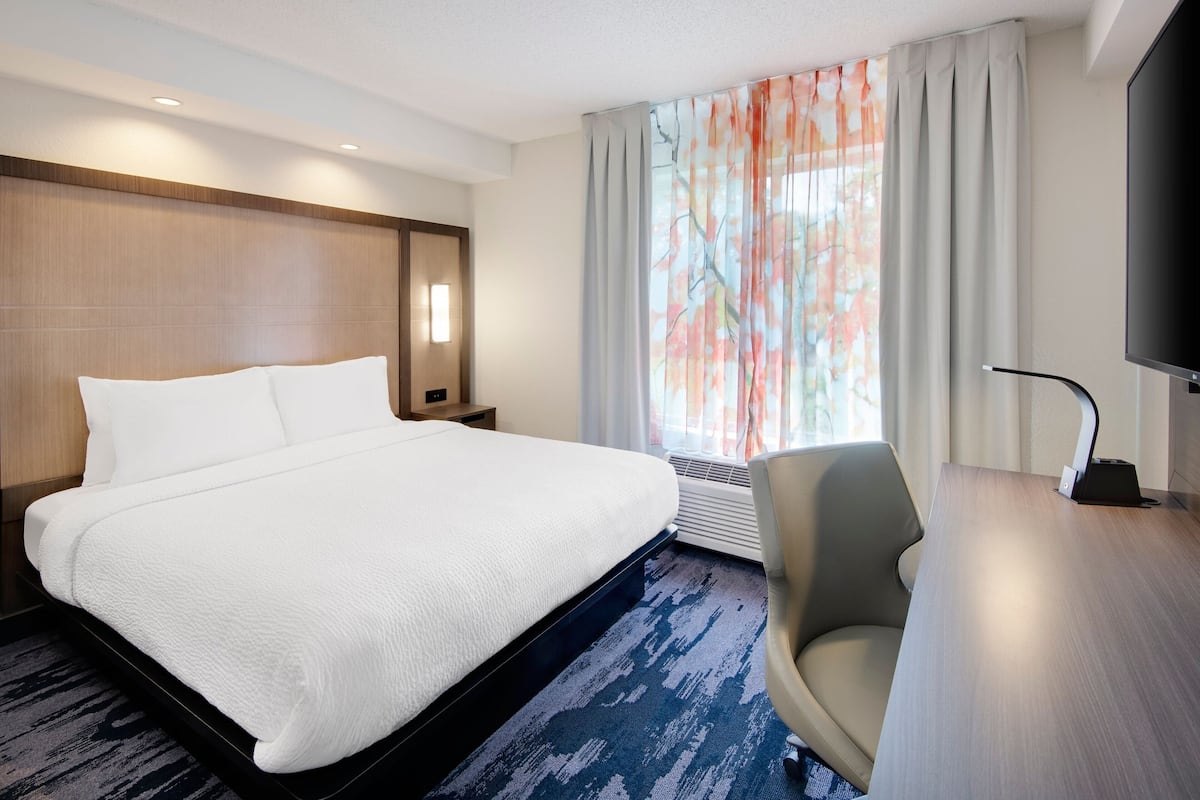 A hotel room with a large bed, a desk with a chair, a flat-screen TV, and a window with curtains.