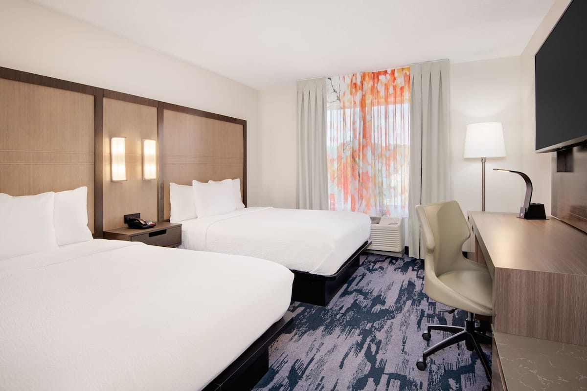 A hotel room with two beds, a desk, a chair, a TV, and a window with curtains.