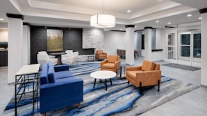 A modern lobby with a blue and gray patterned carpet, white sofas, and a round coffee table. - Fairfield Inn & Suites by Marriott Wilson (Wilson)
