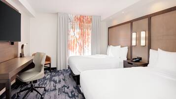 A hotel room with a bed, a desk, a chair, a TV, and a nightstand with a phone.