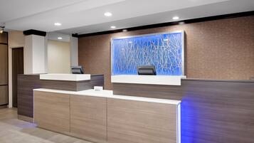 Un área de recepción con diseño moderno, que incluye un mostrador de recepción, una pantalla digital en la pared y un revestimiento mural con diseño.