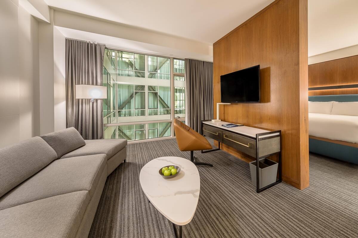 Une chambre d’hôtel équipée d’un canapé, d’un bureau, d’une télévision, d’un lit et d’une fenêtre avec des rideaux.