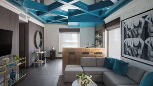 A modern living room with a sofa, coffee table, and a TV. There is a kitchen area with a bar and stools. - Andaz San Diego, by Hyatt (San Diego)