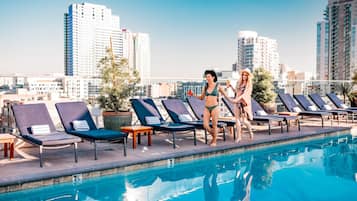 A rooftop pool area with lounge chairs and a clear view of the city skyline.