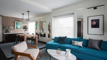 Uma sala moderna com um sofá azul, uma mesa de jantar de madeira e uma área de cozinha com parede de tijolos.