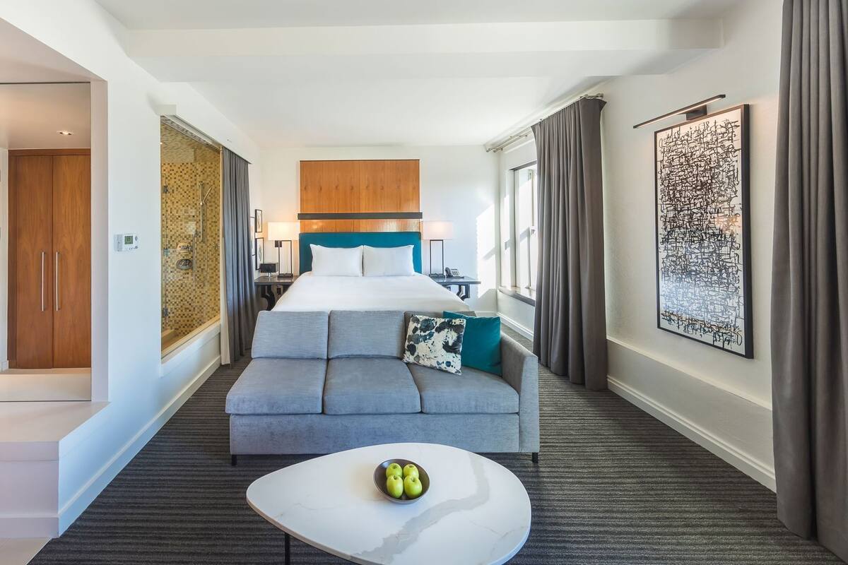 Une chambre d’hôtel avec un lit, un canapé, une table basse avec des pommes, une douche et une salle de bain.