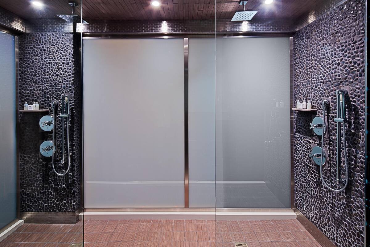 A modern bathroom with a glass shower enclosure, stone-textured walls, and a tiled floor.