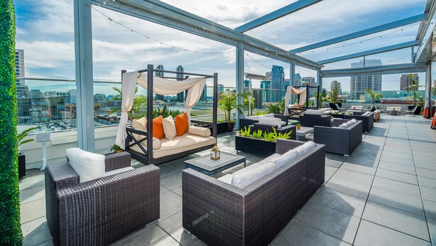 A rooftop lounge with wicker furniture, a canopy bed, and city views. - Andaz San Diego, by Hyatt (San Diego)