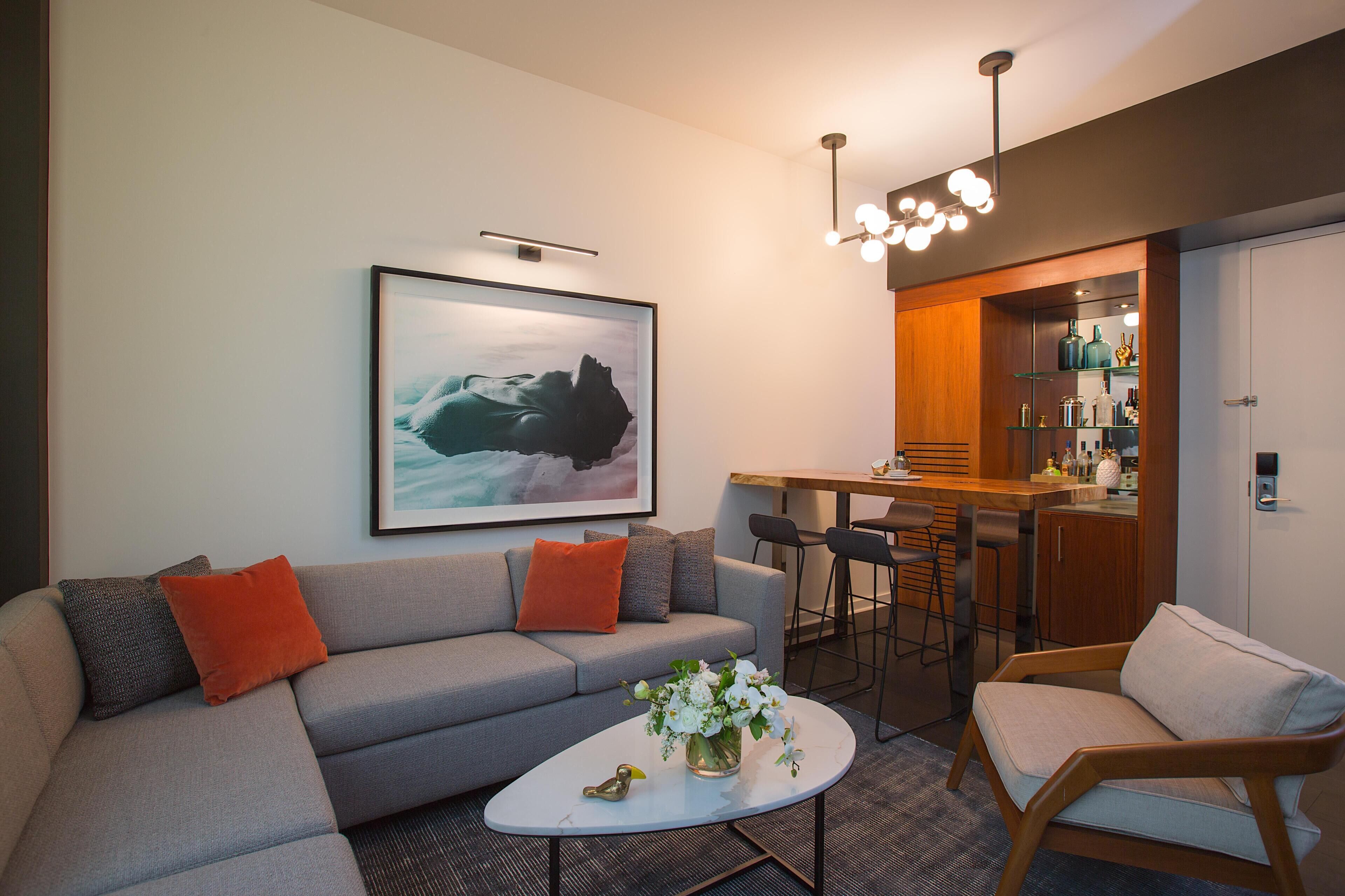 A modern living room with a grey sofa, a coffee table with a vase of flowers, and a framed artwork on the wall.