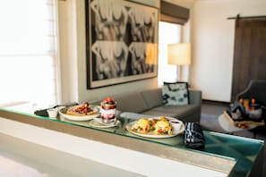 A dining area with a glass table displaying breakfast items, a sofa, a lamp, and a framed picture on the wall. - Andaz San Diego, by Hyatt (San Diego)