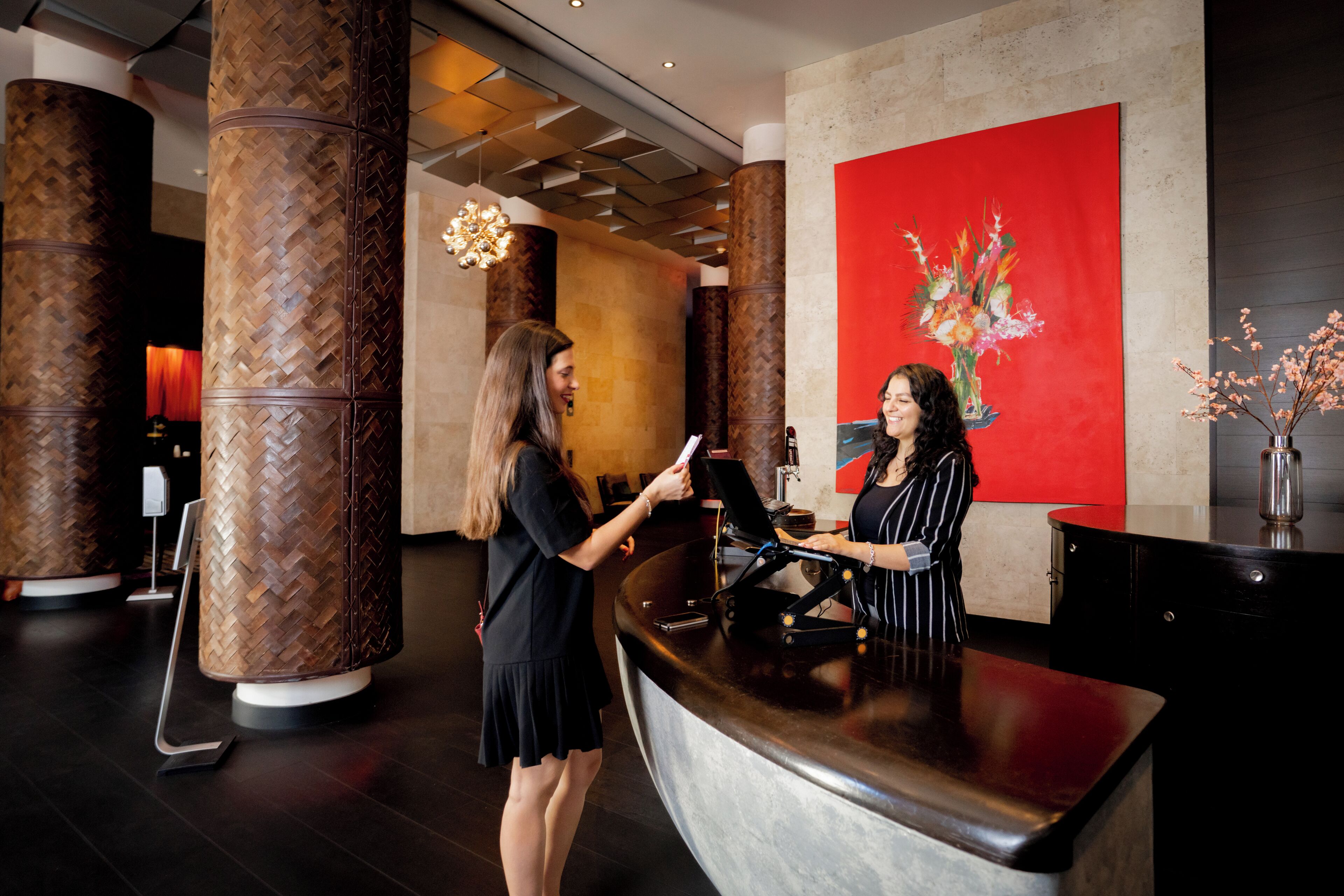 A reception area with a modern design, featuring a large red artwork on the wall, a reception desk, and decorative pillars.