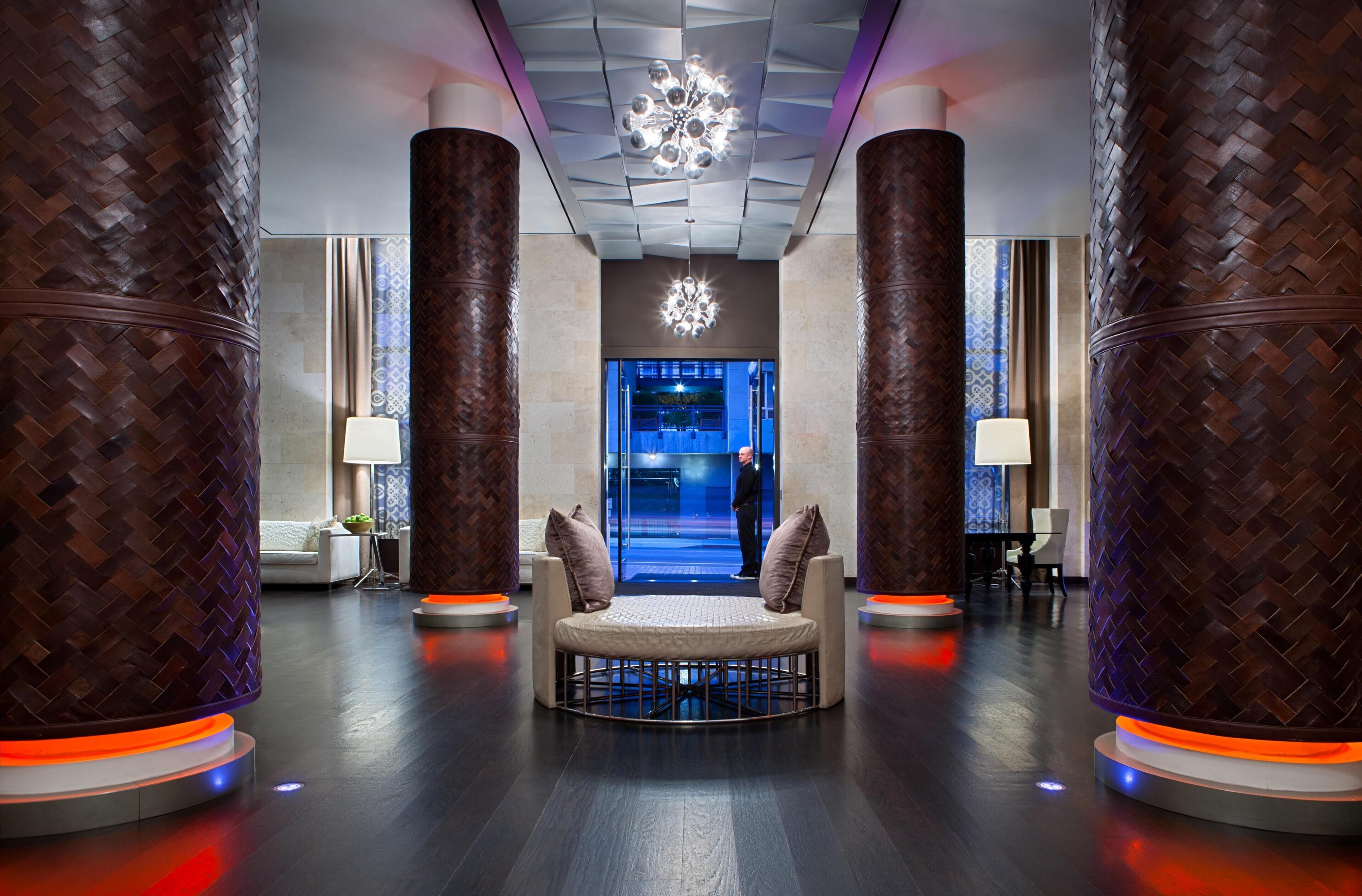 A modern lobby with a central seating area, large wooden columns, and a decorative ceiling light.