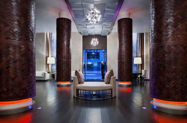 Un vestíbulo moderno con una zona de estar central, grandes columnas de madera y una lámpara decorativa en el techo.