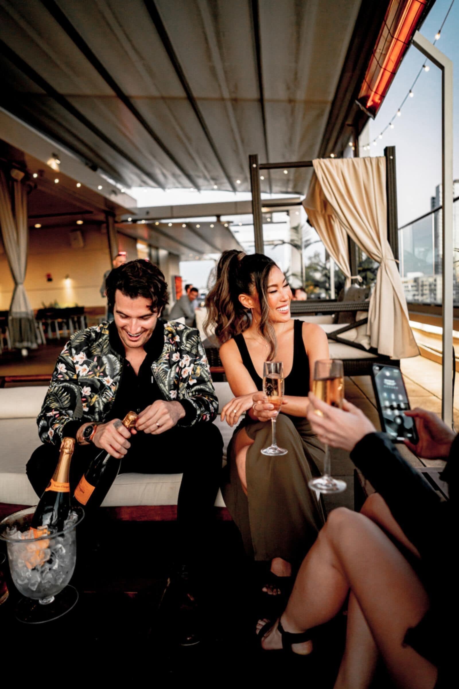 A group of people sitting on a couch, holding champagne glasses, with a city view in the background.