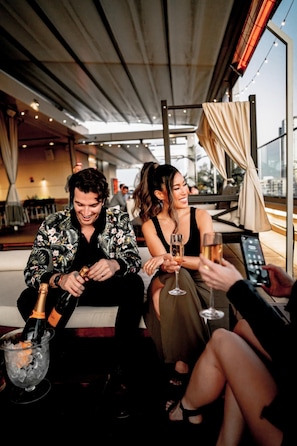 A group of people sitting on a couch, holding champagne glasses, with a city view in the background.
