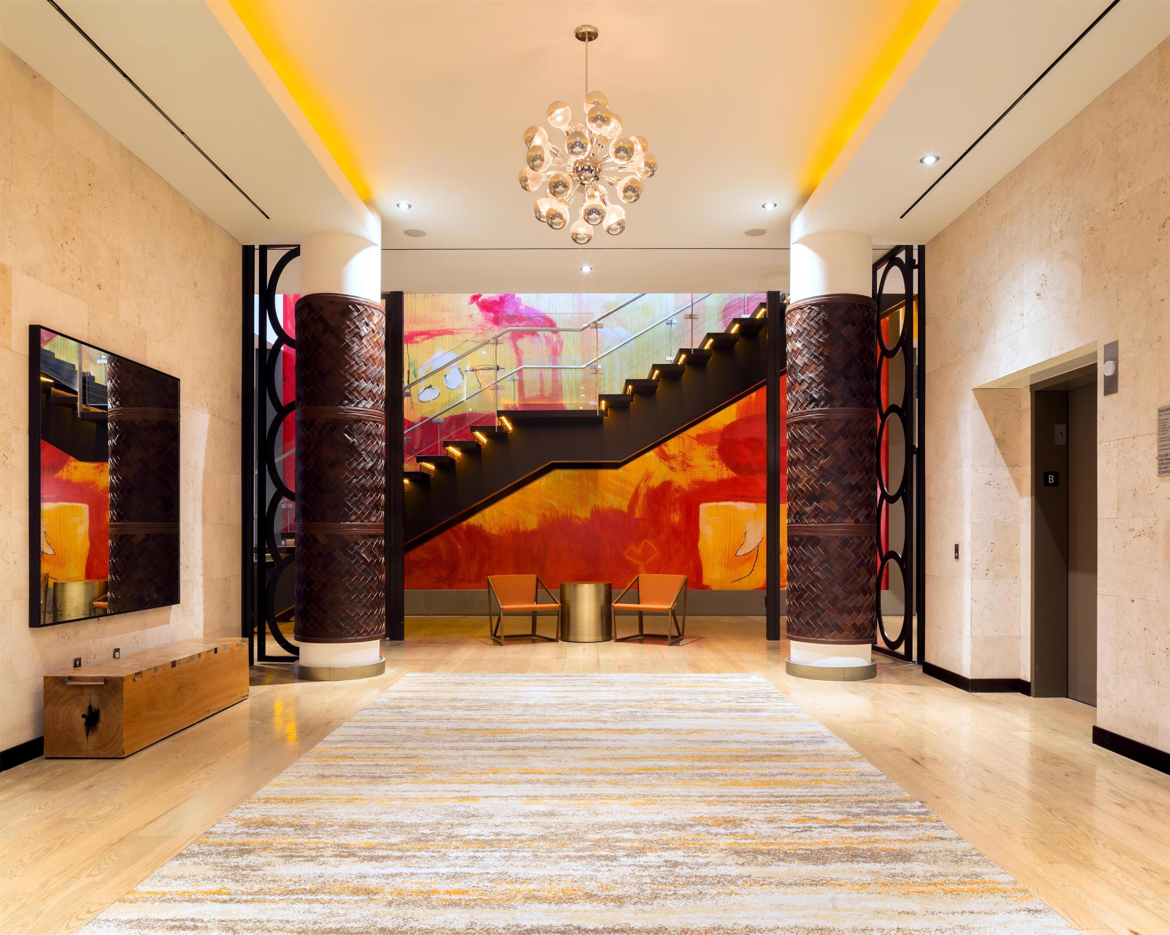 A hotel lobby with a staircase, a chandelier, and a large abstract painting.