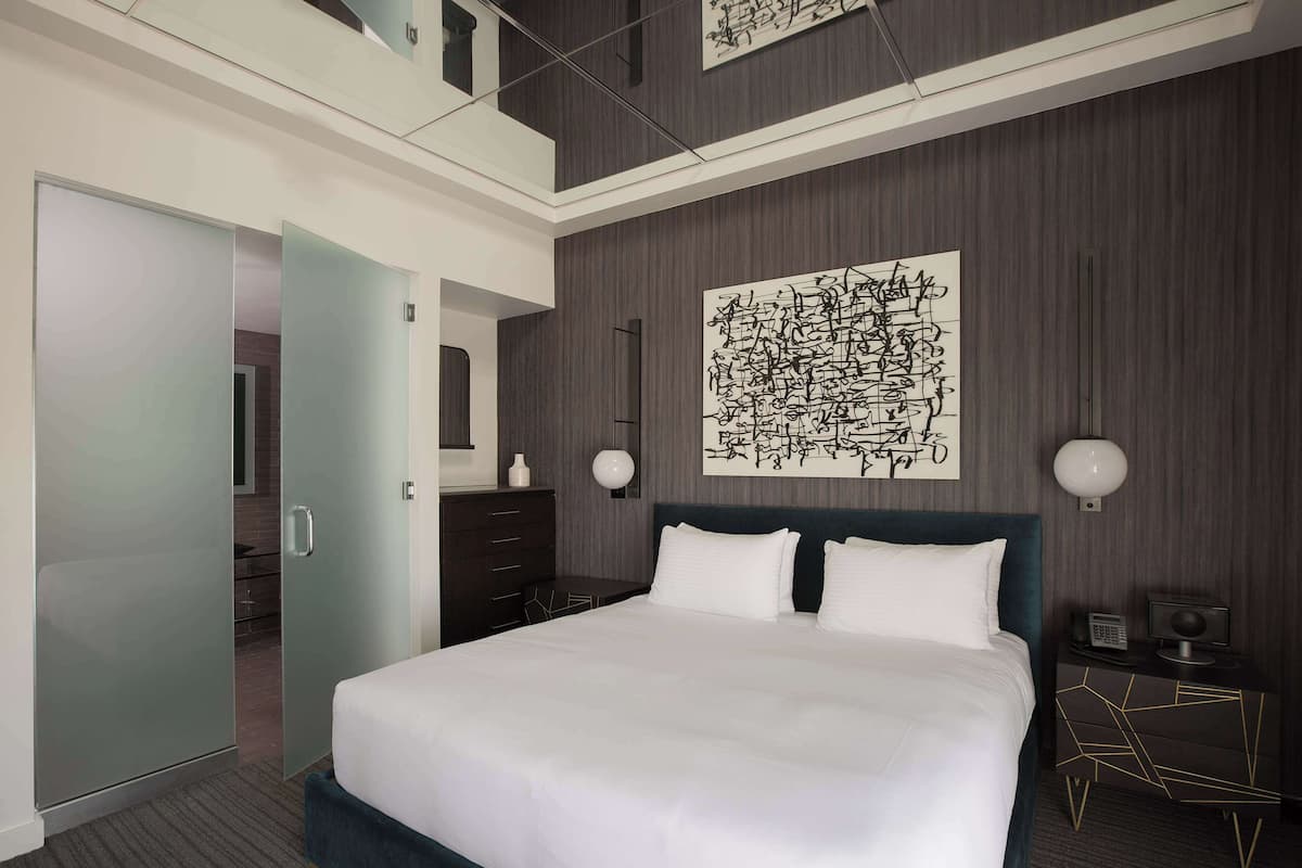 Une chambre d’hôtel moderne avec un grand lit, une armoire, un bureau avec une lampe et une œuvre d’art murale.