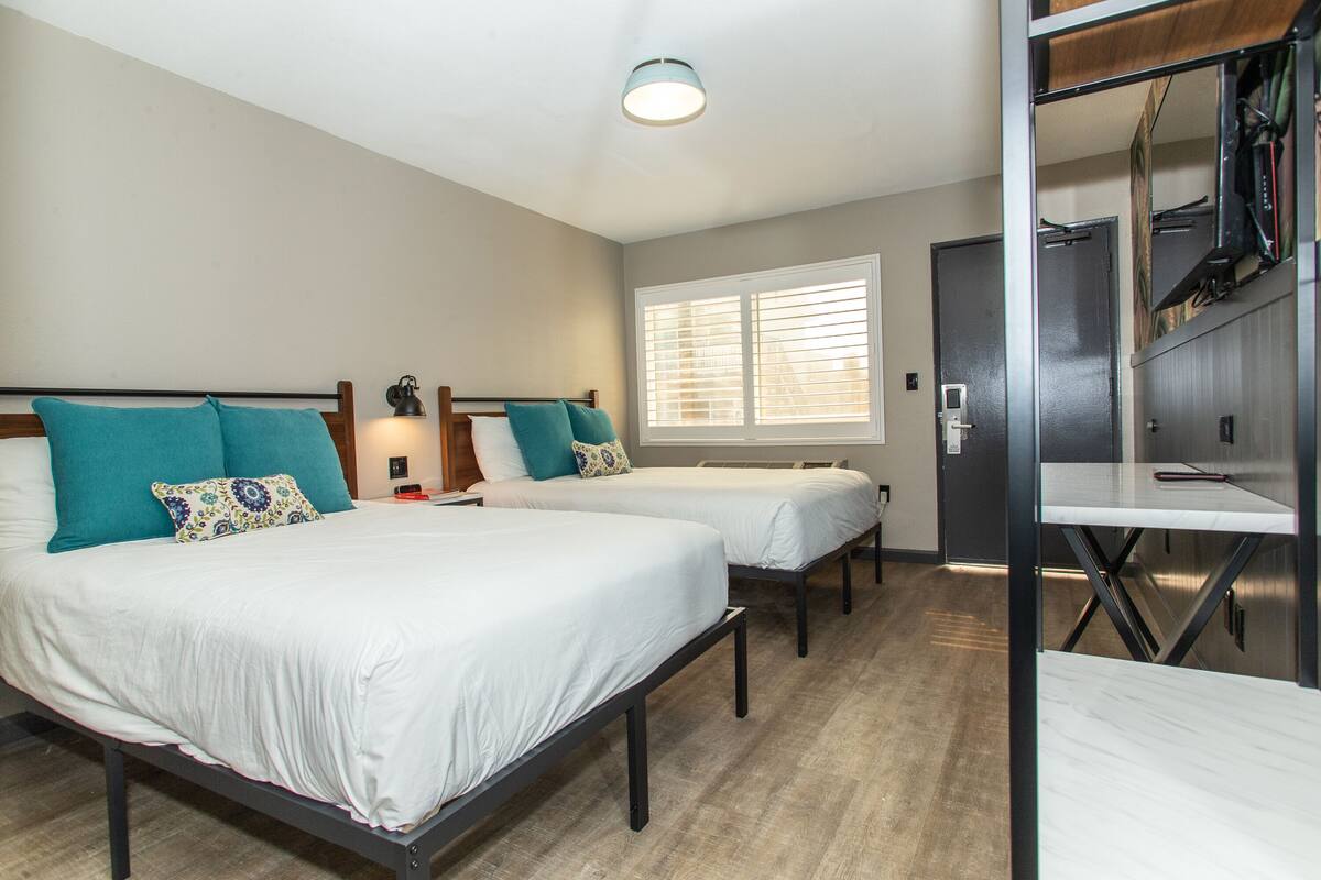 A bedroom with two beds, a window with blinds, a desk, and a wardrobe.