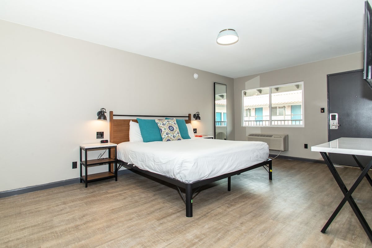 A modern hotel room with a bed, bedside tables, a desk, and a TV.