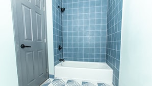 A bathroom with a white bathtub, blue tiled walls, and a geometric patterned floor. - Magnolia Tree Hotel - Near Anaheim Convention Center (Anaheim)
