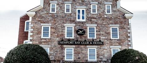 A historic stone building with a sign for Newport Bay Club & Hotel and Perry Mill Market.