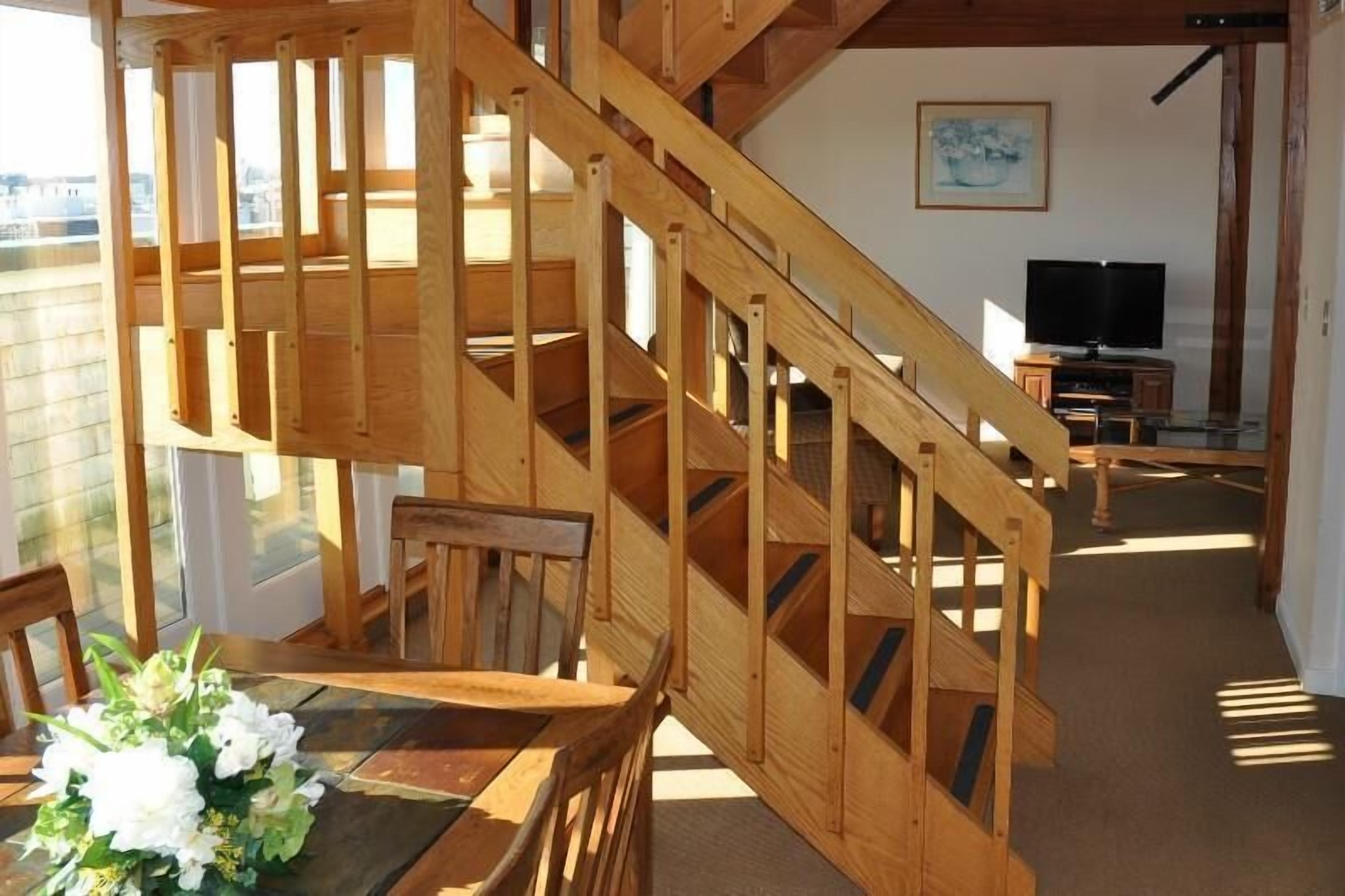 Un escalier en bois mène à un balcon, en dessous duquel se trouve un espace repas.