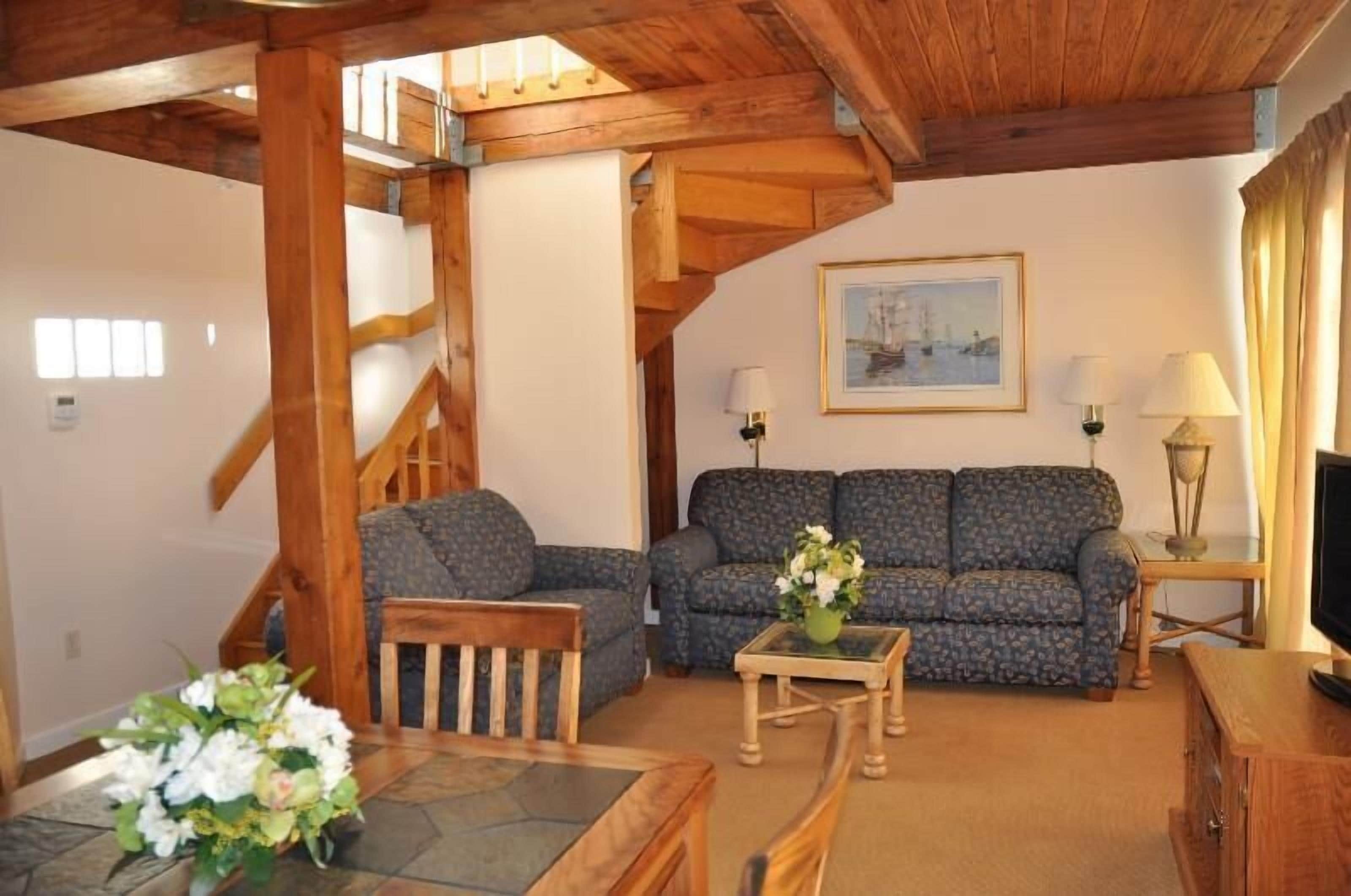 A cozy living room with a wooden staircase, a sofa, a coffee table, and a TV.