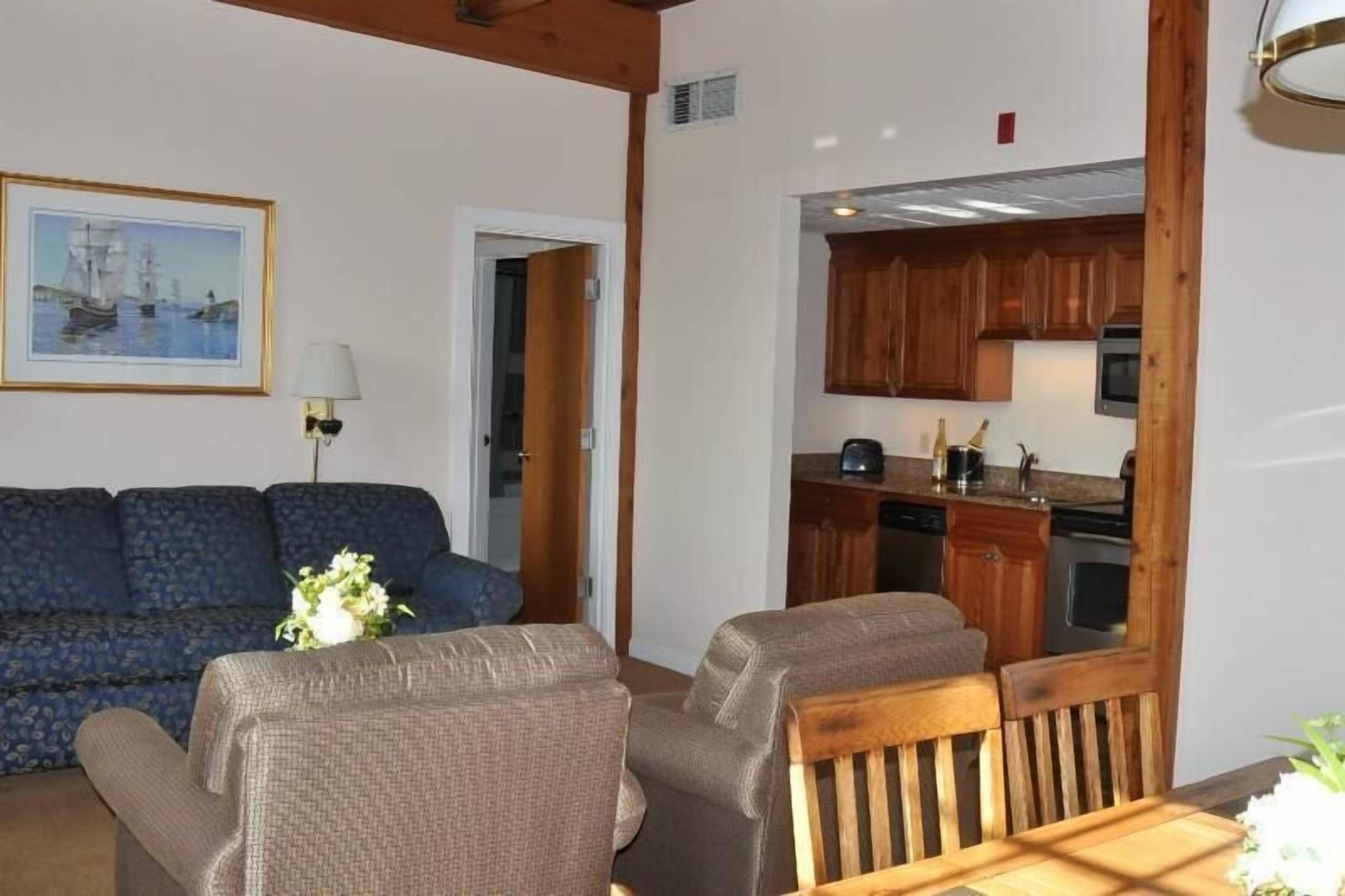 A living room with a sofa, two armchairs, a dining table, and a kitchen area with wooden cabinets and appliances.