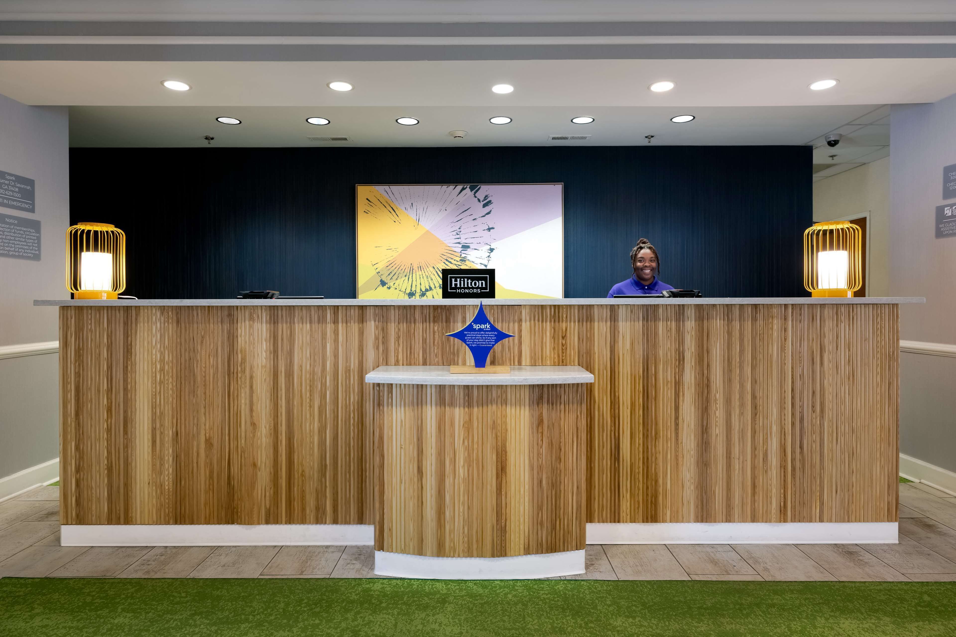 A reception desk with a wooden finish, a Hilton Honors logo, and two illuminated wall sconces.