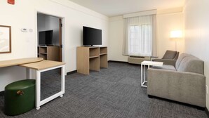 Une chambre d’hôtel équipée d’une télévision à écran plat, d’un canapé, d’une petite table et d’une fenêtre avec des rideaux.