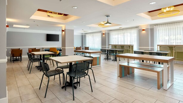 Un vaste espace dédié à la salle à manger, avec de nombreuses tables et chaises, un éclairage encastré au plafond et de grandes fenêtres.