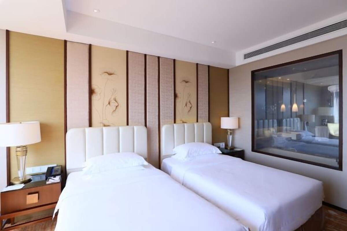 Een hotelkamer met twee bedden, een groot raam en een decoratief wandpaneel.