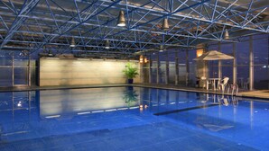 An indoor swimming pool with a blue tiled floor, metal beams on the ceiling, and a seating area with tables and chairs. - Howard Johnson Pearl Plaza Wuhan (Wuhan)