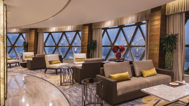 A modern hotel lobby with a curved marble reception desk, comfortable seating areas, large windows with a view, and decorative plants. - Howard Johnson Pearl Plaza Wuhan (Wuhan)