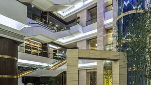 A multi-level atrium with a grand staircase, seating area, and a large cylindrical water feature. - Howard Johnson Pearl Plaza Wuhan (Wuhan)