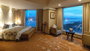 A hotel room with a large bed, a sitting area with a chair and table, and a view of a cityscape through large windows. - Howard Johnson Pearl Plaza Wuhan (Wuhan)