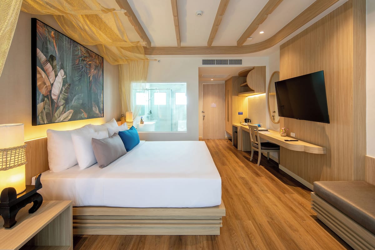 Una habitación de hotel moderna con una cama grande, un escritorio, un televisor de pantalla plana y un amplio ventanal con vistas al exterior.