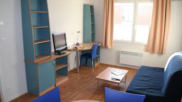 A compact room with a desk, computer, chair, and a sofa.