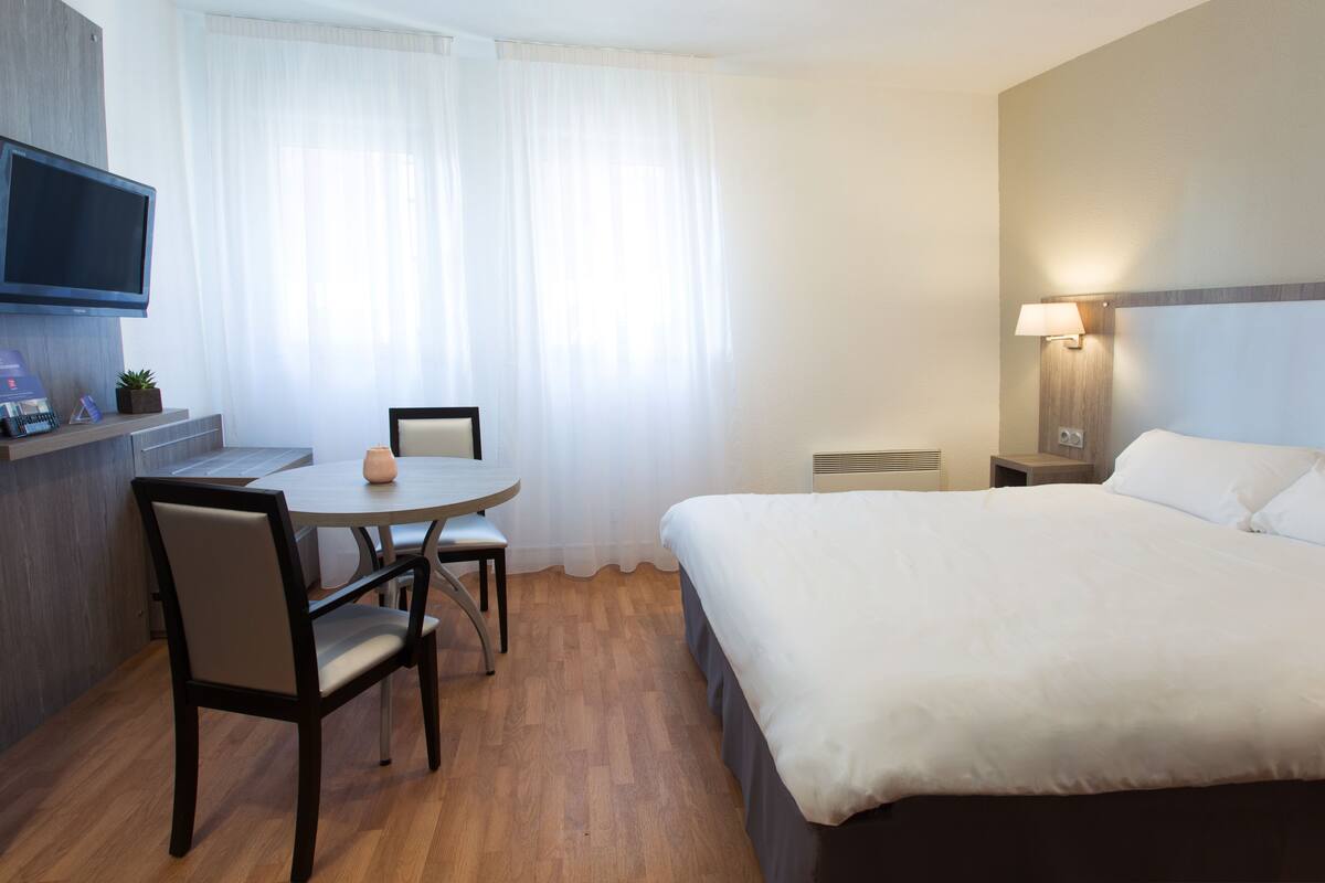 Une chambre d’hôtel comprenant un lit, un bureau avec une chaise, une télévision et une lampe.